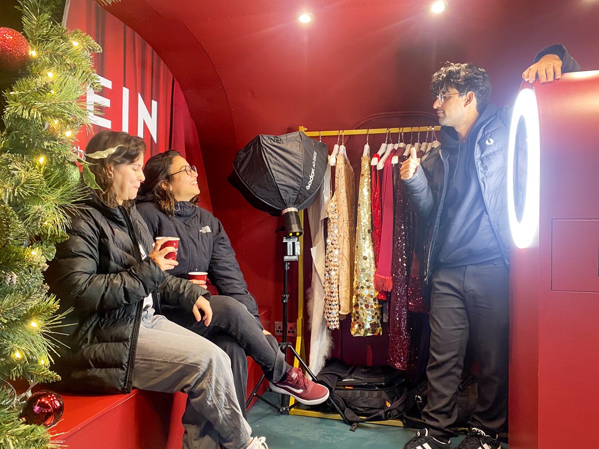 A staff member readies two guests as they pose at SHEIN's branded photo moment, with light ring and booth.