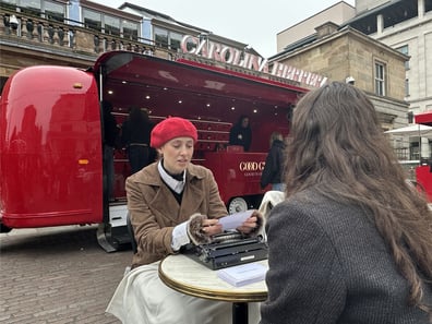 Two women sit near Carolina Herrera's red Airstream trailer in London.