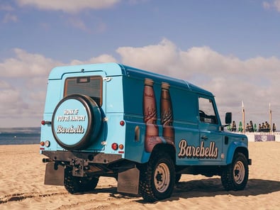 The custom sampling vehicle, a classic Land Rover Defender in blue, on a beach for an event.