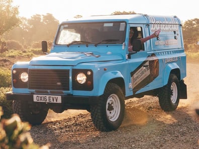 Driving the blue custom Land Rover Defender on rough terrain for a promotional campaign or brand activation.