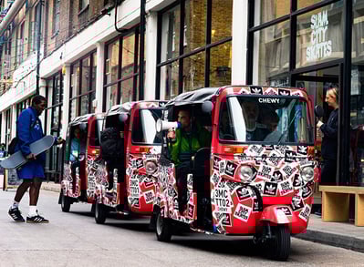 3 red promotional tuk tuk hires, with a staff member using a megaphone