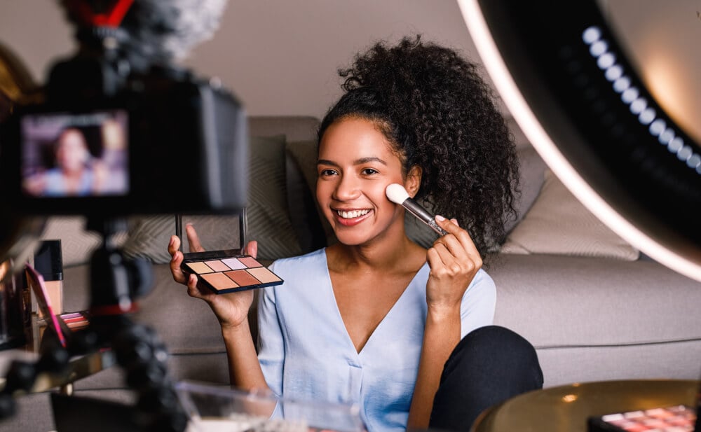A beauty influencer films herself applying make-up as part of a promotional video.