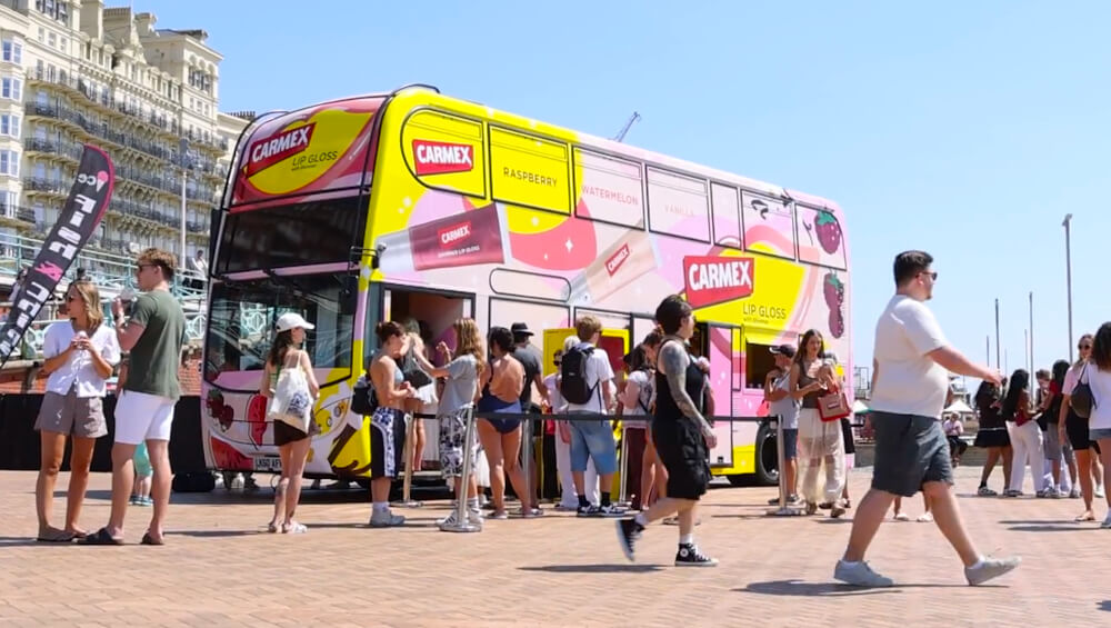Carmex double-decker Shimmer Lip Gloss bus with a large crowd in summer.