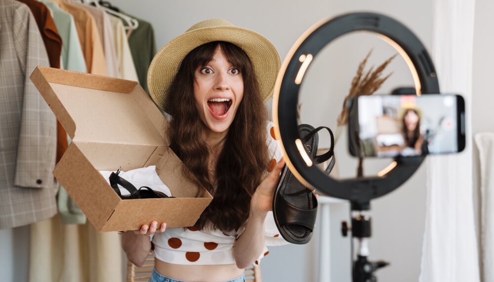 A nano influencer is excited to open a shoe box on camera, with ring light.