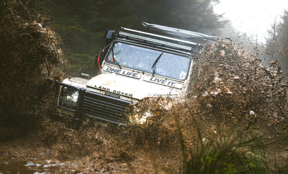 A classic Land Rover Defender travelling through mud in the countryside.