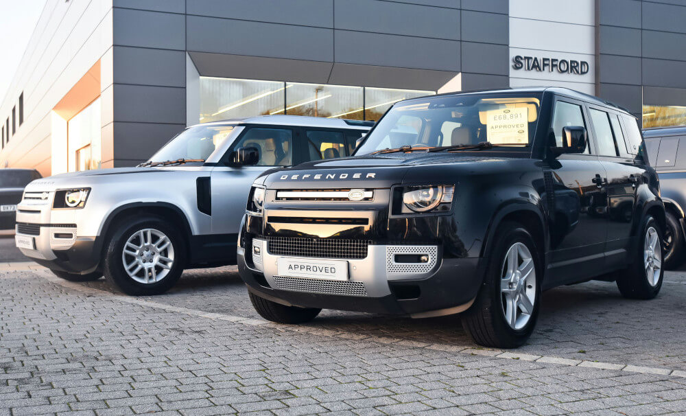 Two modern Land Rover Defenders at a car lot.