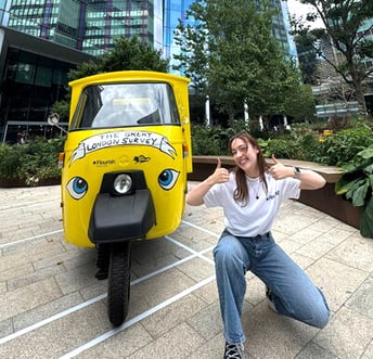 A front view of the Data Vandals and Canva 'data week' Piaggio Ape, with a woman posing looking happy in London.