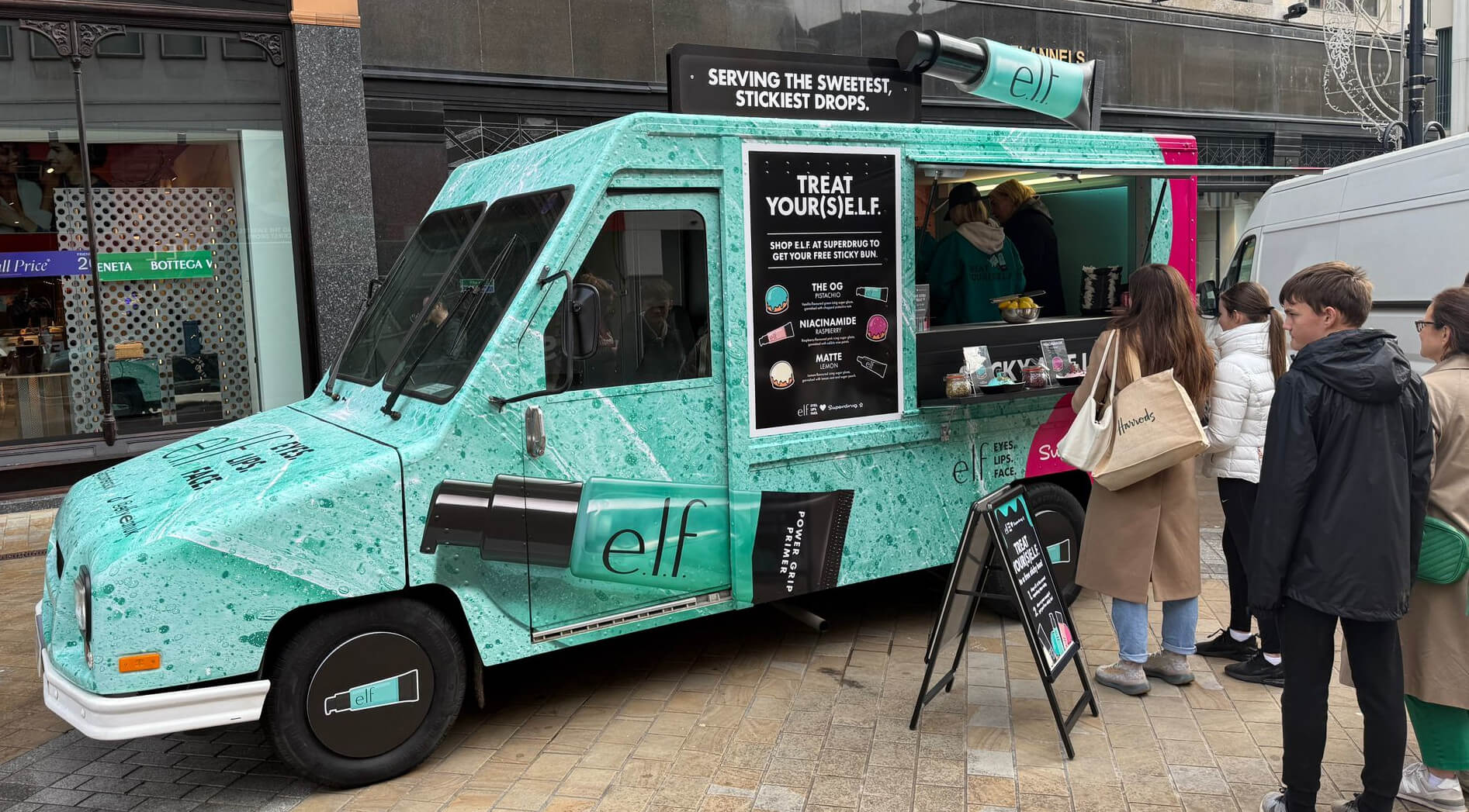 A crowd gathers at the E.L.F. and Superdrug beauty brand event, with a promotional post van.