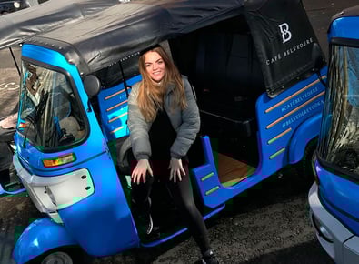 The side of the blue Belvedere custom tuk tuk, with a woman smiling inside