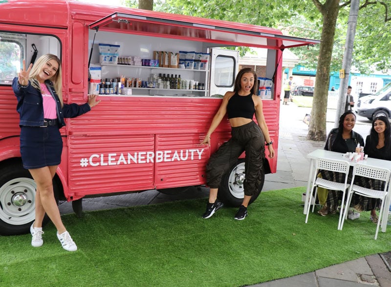 Two young women pose with a Citroen H Van at a brand activation, with product sampling displays.