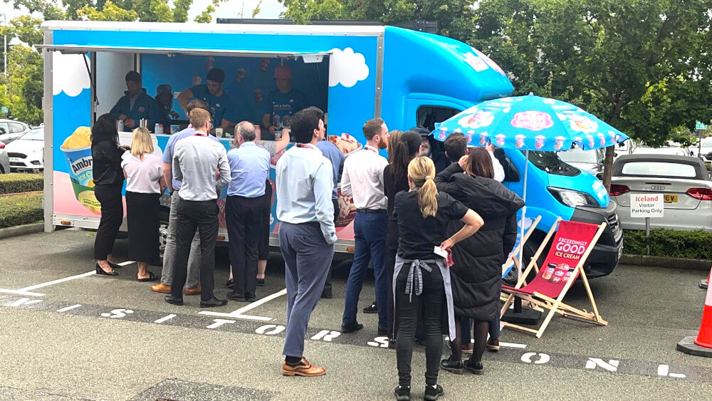 A crowd by the Premier Foods mobile food van, with staff at work inside and a branded chair and umbrella for the food activation.