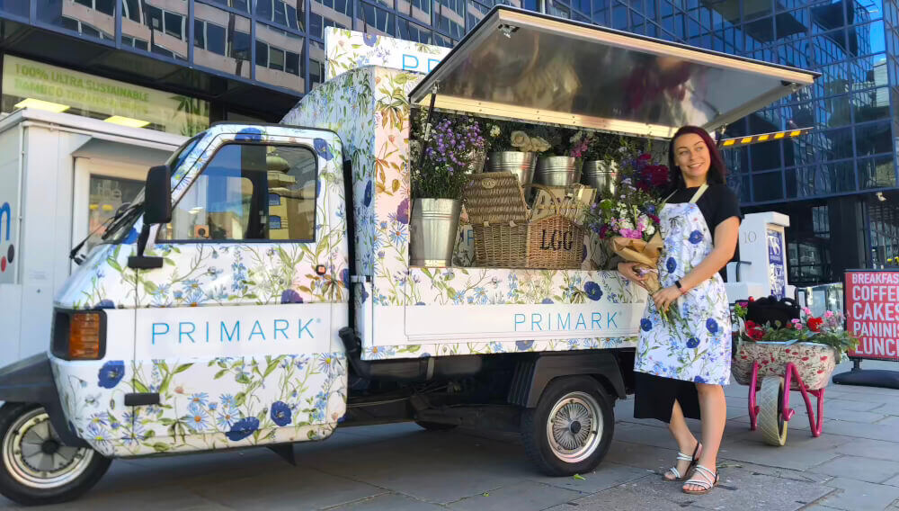 Primark's Piaggio Ape with a young woman holding flowers as part of a PR stunt.