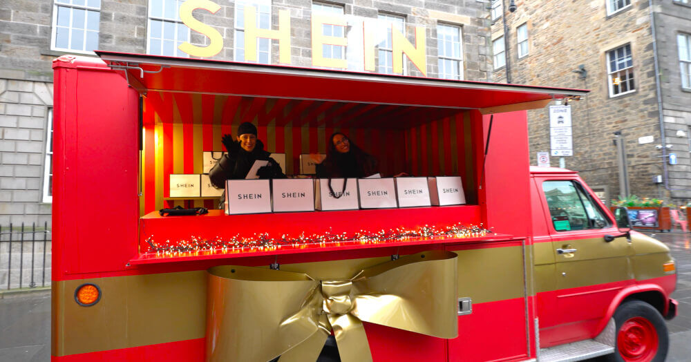A red promotional ambulance with a gold bow, with two staff members at a Christmas brand activation.