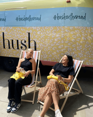 customers relaxing in Hush branded deckchairs next to vintage blue and yellow hush branded Airstream