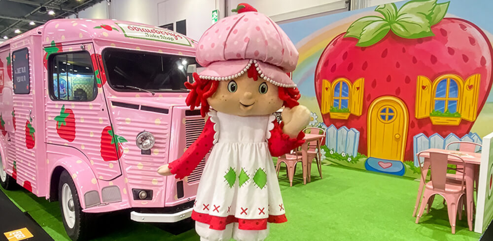 Strawberry Shortcake poses in front of an apple background and the pink, custom Citroen H-Van.