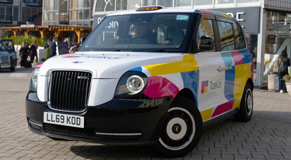 An electric taxi hire driving near a shopping centre in London