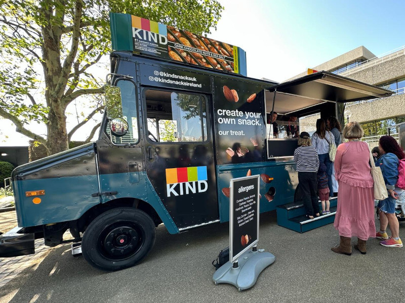An image of the KIND Snacks Toppings Tour promotional step van, with branding and roof sign in London as part of a sampling campaign.