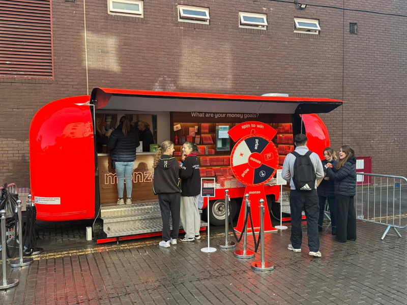 A promotional Airstream with the interior open and a young crowd gathered for the brand Monzo.