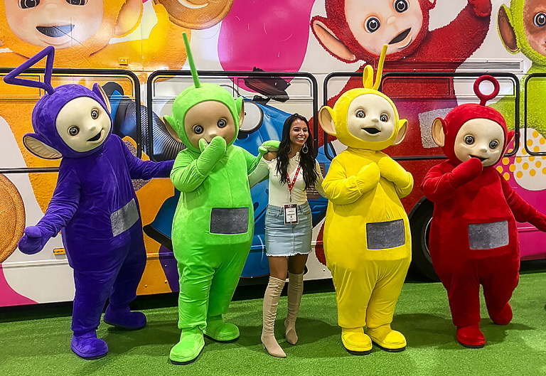 An image of the Teletubbies and a woman smiling, stood in front of their brand awareness campaign bus.