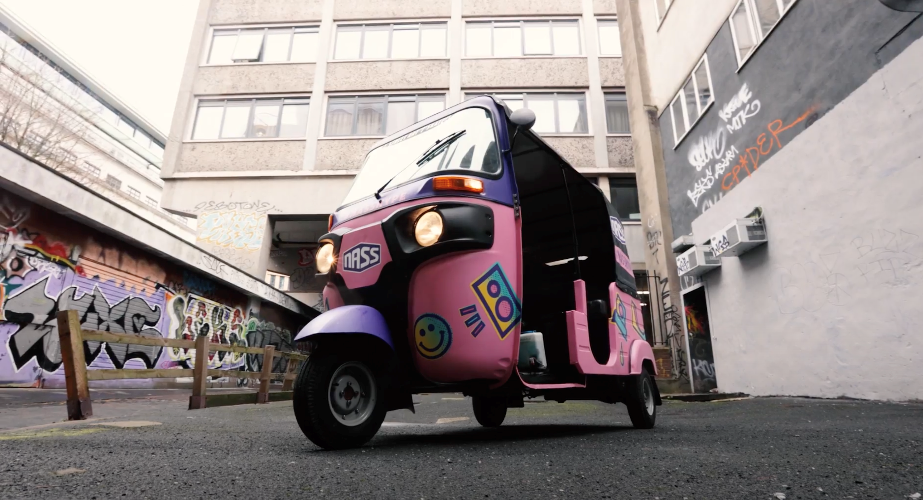 The NASS branded promotional tuk tuk hire, with the headlights on.